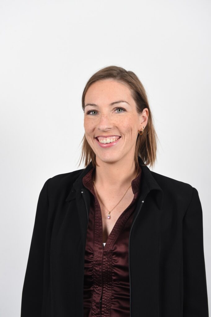 Delphine Smagghe smiling in a professional portrait, wearing a dark blouse against a neutral background.