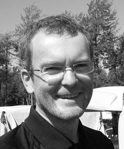 Portrait of Yannick Marcon wearing glasses and smiling outdoors.